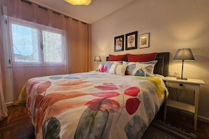 A hotel room with a bed, a nightstand, a lamp, and a window with curtains.