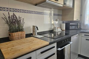 A kitchen with a wooden cutting board, a kettle, a microwave, and a stove.