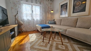 A living room with a sofa, a glass coffee table, a lamp, and a TV on a wooden cabinet. - 645A Coqueto apartamento en Oviedo (Oviedo)