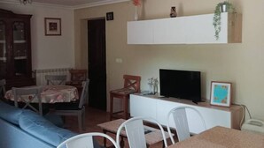 Een woonkamer met een bank, een eettafel, stoelen, een televisie en een kast.