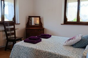 A bedroom with a bed, a wooden chair, a dresser, and a mirror.