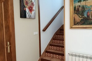 Un escalier orné de carreaux décoratifs, une main courante en bois, une porte avec une poignée en laiton et deux œuvres d’art encadrées accrochées aux murs.