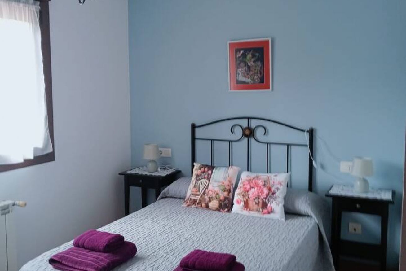 Ein Schlafzimmer mit einem Bett, zwei Nachttischen, einem Fenster mit Vorhängen und einem gerahmten Bild an der Wand.