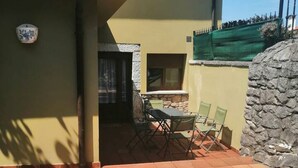 Een terras buiten, met een tafel, stoelen, een stenen muur en een raam met uitzicht.