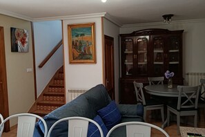 A living room with a sofa, chairs, a dining table, and a staircase. - 13A05 La Casina en Sebreño (Ribadesella)