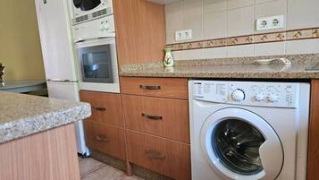 Une cuisine équipée d’un lave-linge, d’un four et de meubles de rangement en bois.