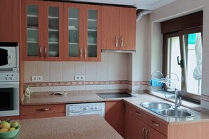 A kitchen with wooden cabinets, a microwave, an oven, a dishwasher, and a sink. - 13A05 La Casina en Sebreño (Ribadesella)
