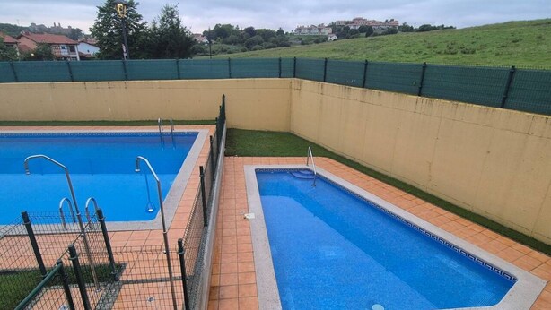A swimming pool with two separate sections, surrounded by a fence and a tiled deck.