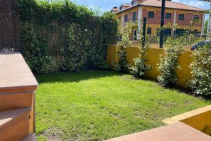 A backyard with a grassy lawn, a yellow wall, and a fence.