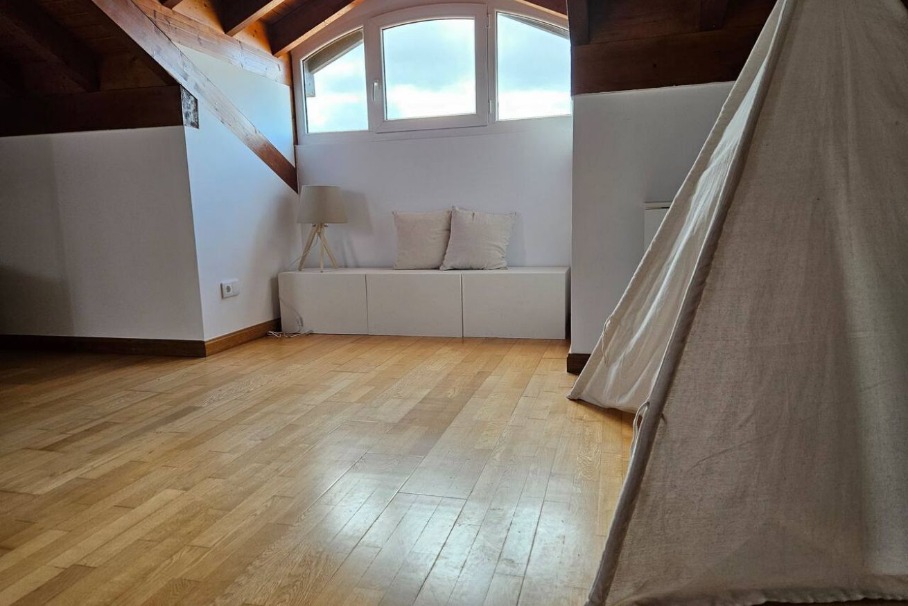 Una habitación con piso de madera, un sofá blanco, una lámpara y una ventana con vistas.