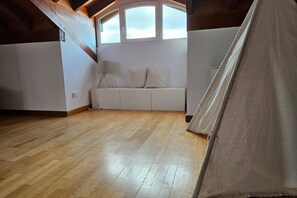 A room with a wooden floor, a white sofa, a lamp, and a window with a view.