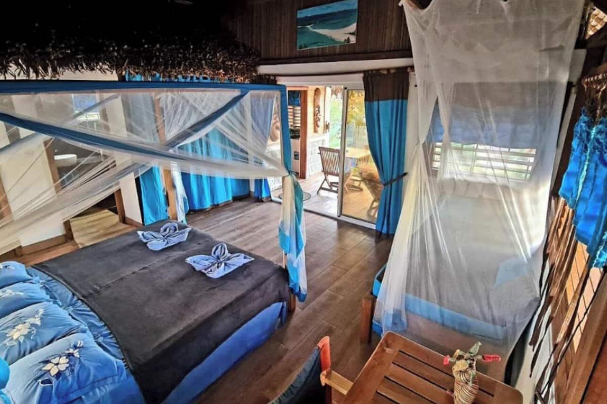 Una habitación con una cama, una mesa de madera y una silla. Hay una ventana con cortinas y vistas al exterior.