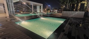 Una piscina con plataforma de baldosas, rodeada de arquitectura moderna y un ambiente nocturno.