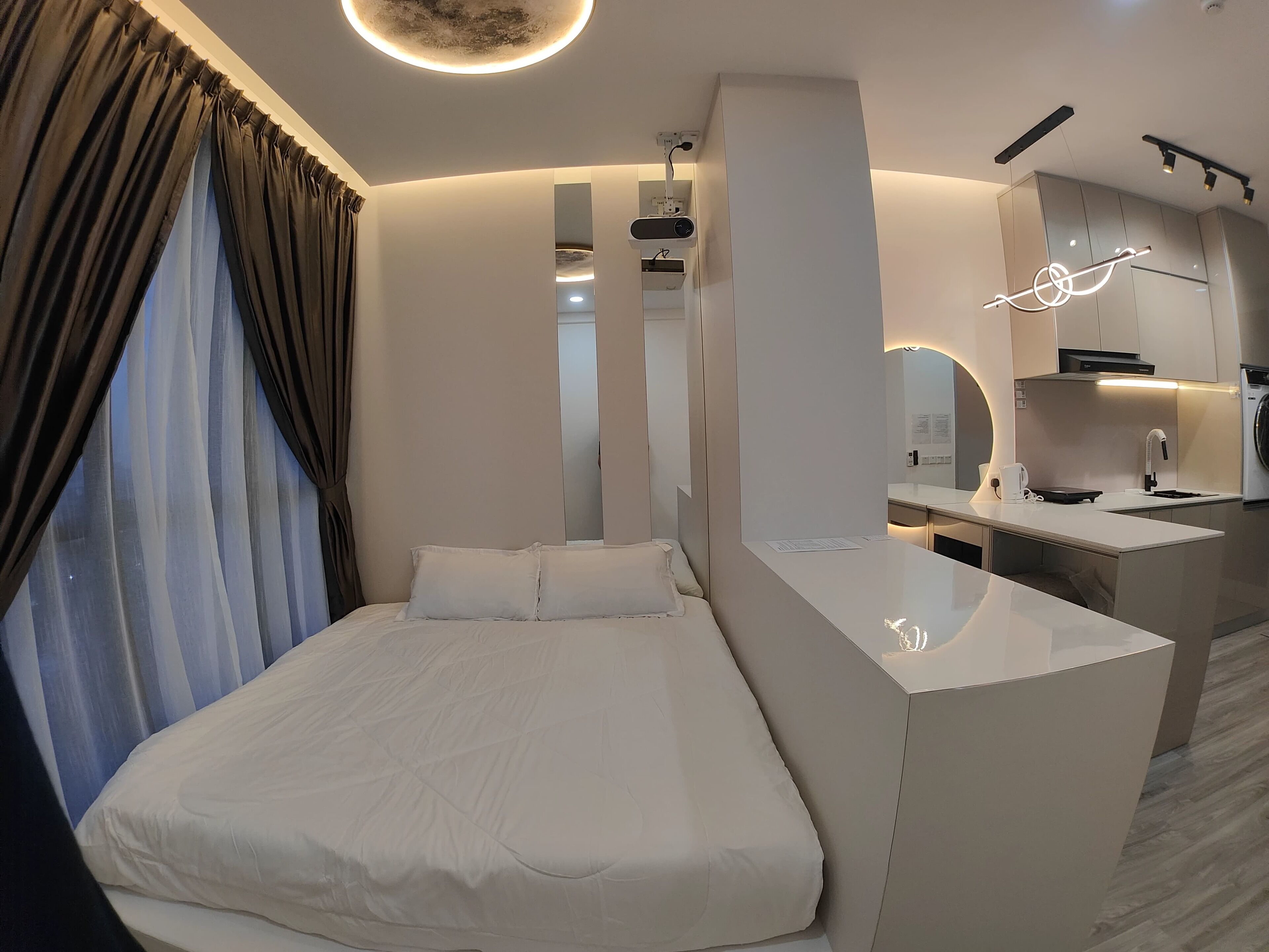 Una habitación de hotel moderna con una cama, una kitchenette pequeña y un baño visible a través de un espejo.