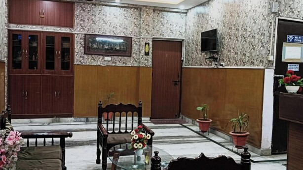 A lobby with a reception desk, a seating area with a chair and table, a wooden cabinet, and a television on the wall. - WoodStock Homestay By GRB (Lucknow)