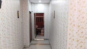 A narrow hallway with patterned wallpaper and a marble floor leading to a room with a wooden door and a small table with a vase. - WoodStock Homestay By GRB (Lucknow)