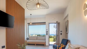 A modern living room with a sofa, a chair, a table, and a large window offering a view of the sea. - KaYa SeaView Residence (Mylopotamos)