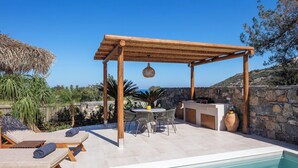 A poolside area with lounge chairs, a pergola, a dining table with chairs, and a stone wall. - KaYa SeaView Residence (Mylopotamos)