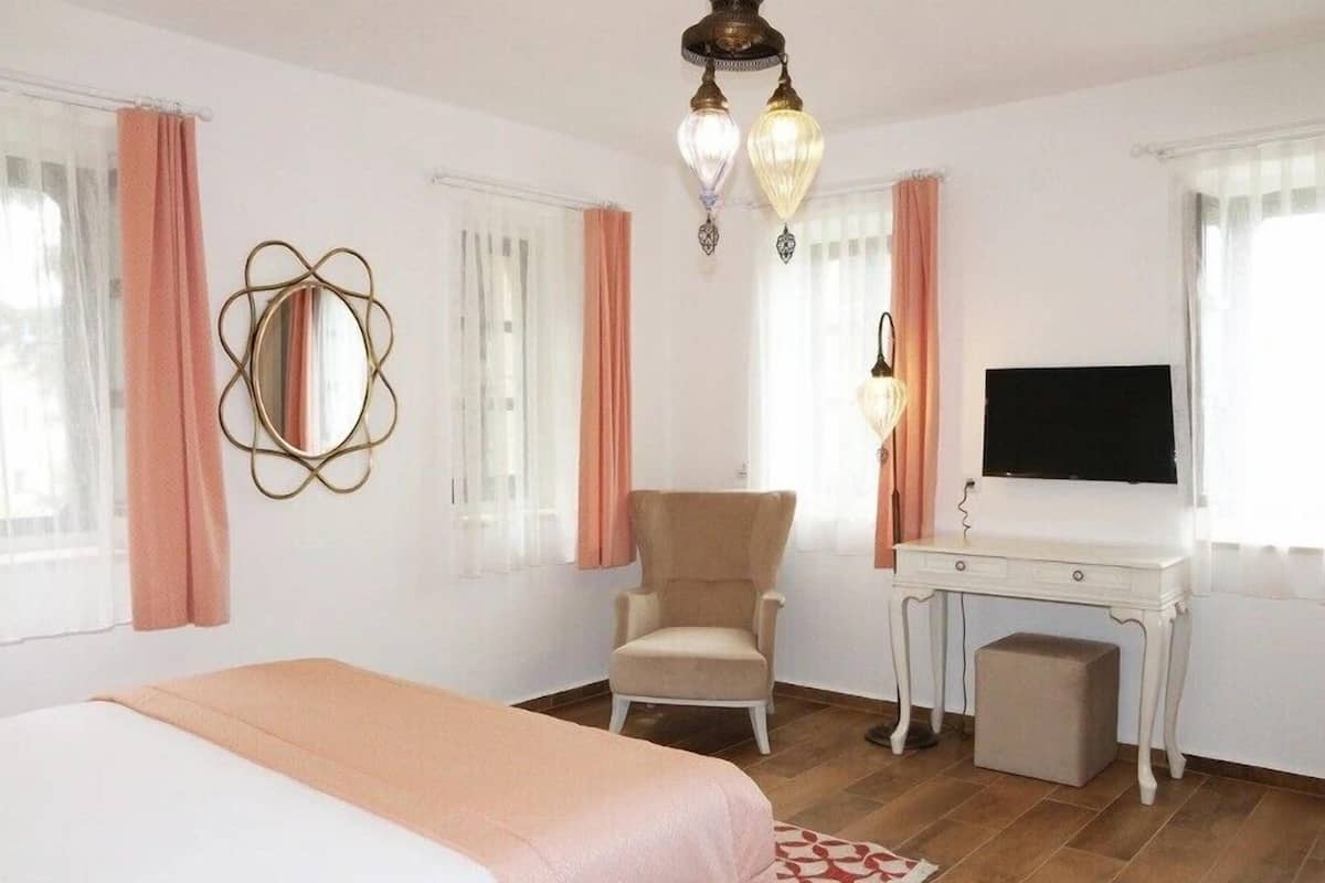 A hotel room with a bed, a desk with a television, a chair, and a decorative mirror.