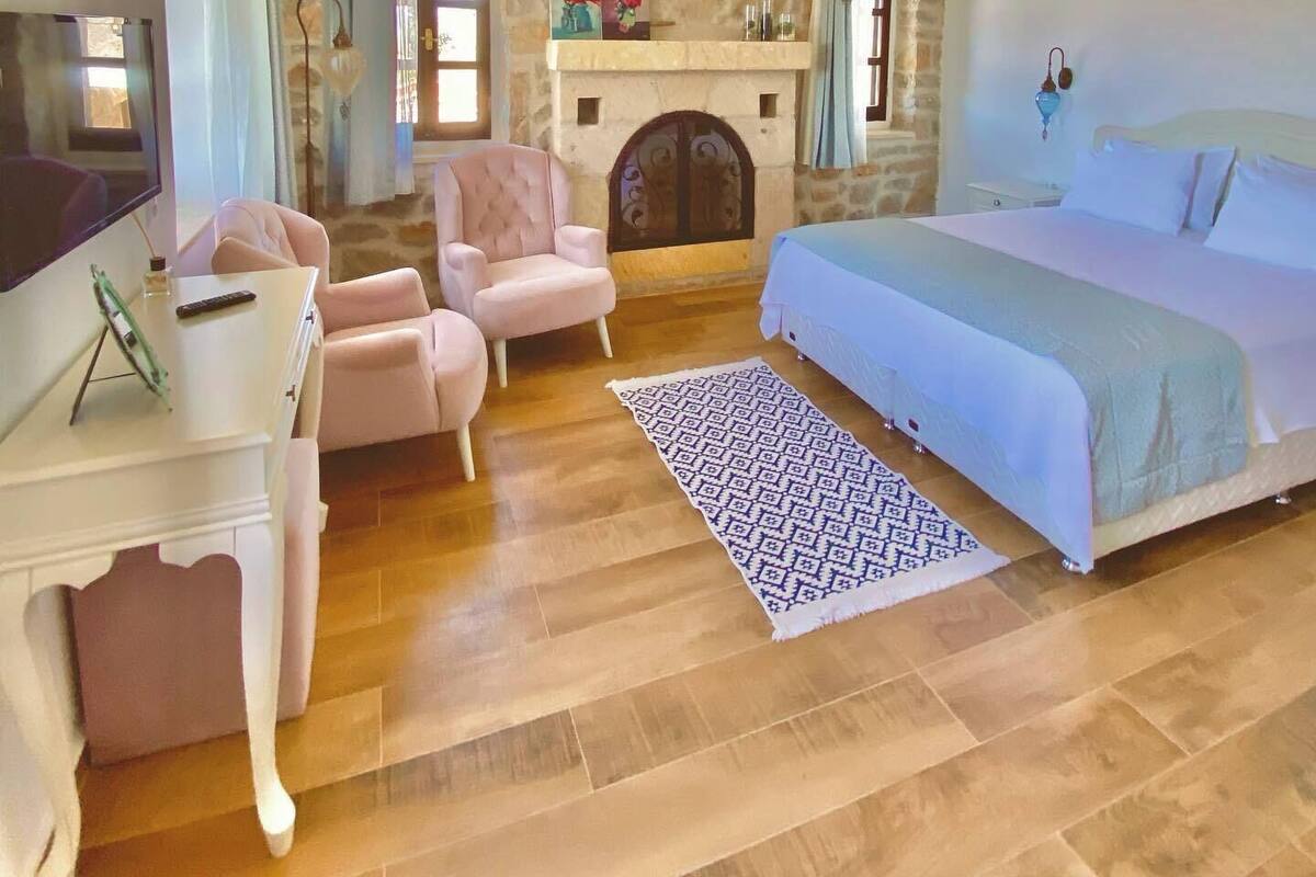 A bedroom with a bed, a television, a fireplace, and a stone wall.