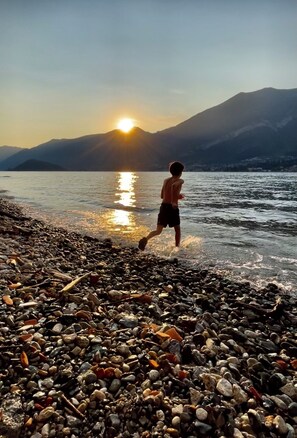 A child running along a pebbled beach with a sunset in the background. - Casa Lory S - Two-Bedroom Penthouse Just Steps from the Lake (Lombardia)