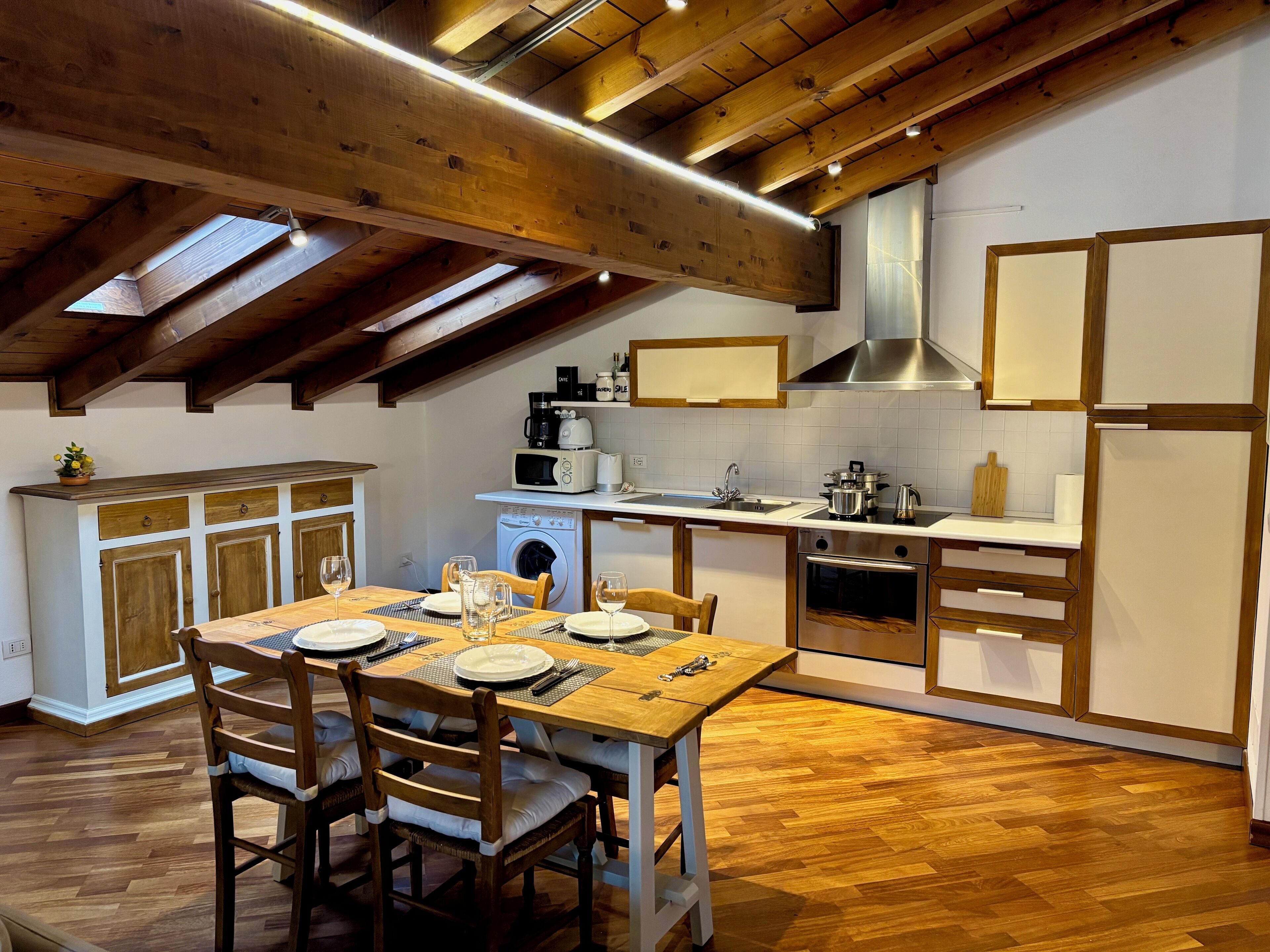 A kitchen with wooden beams, a dining table set for four, and a washing machine.