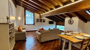Een gezellige loftkamer met houten plafond, een eettafel gedekt voor vier personen en een bank met kussens.