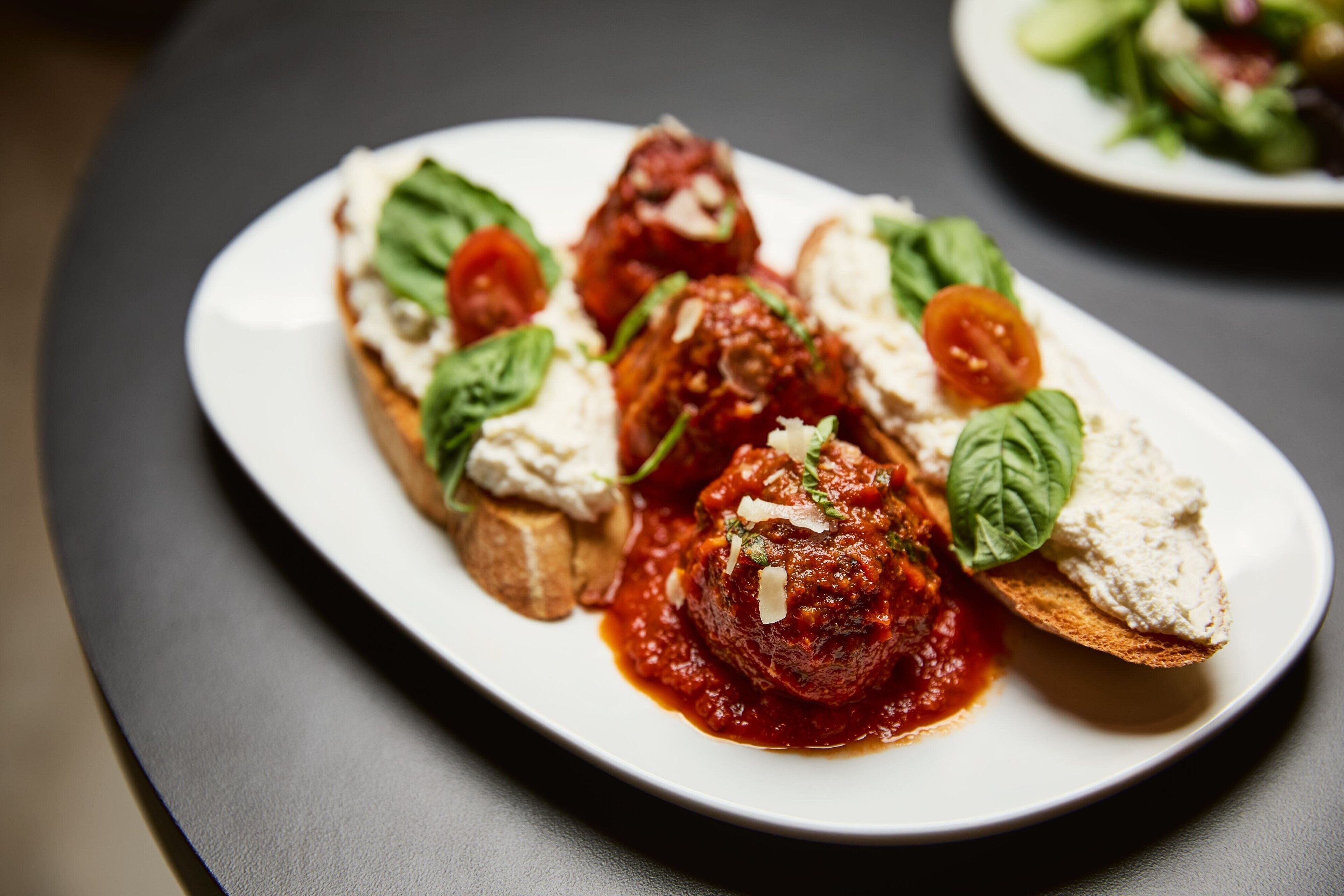 A plate with meatballs in tomato sauce, garnished with basil and cheese, served on a slice of bread.
