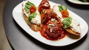 A plate with meatballs in tomato sauce, garnished with basil and cheese, served on a slice of bread.