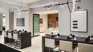 A modern dining area with a long table, multiple chairs, and a bar area with a counter. - AC Hotel by Marriott Kansas City Downtown (Kansas City)