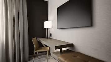 A modern hotel room with a wooden desk, a chair, a bench, a large wall-mounted TV, and a lamp.