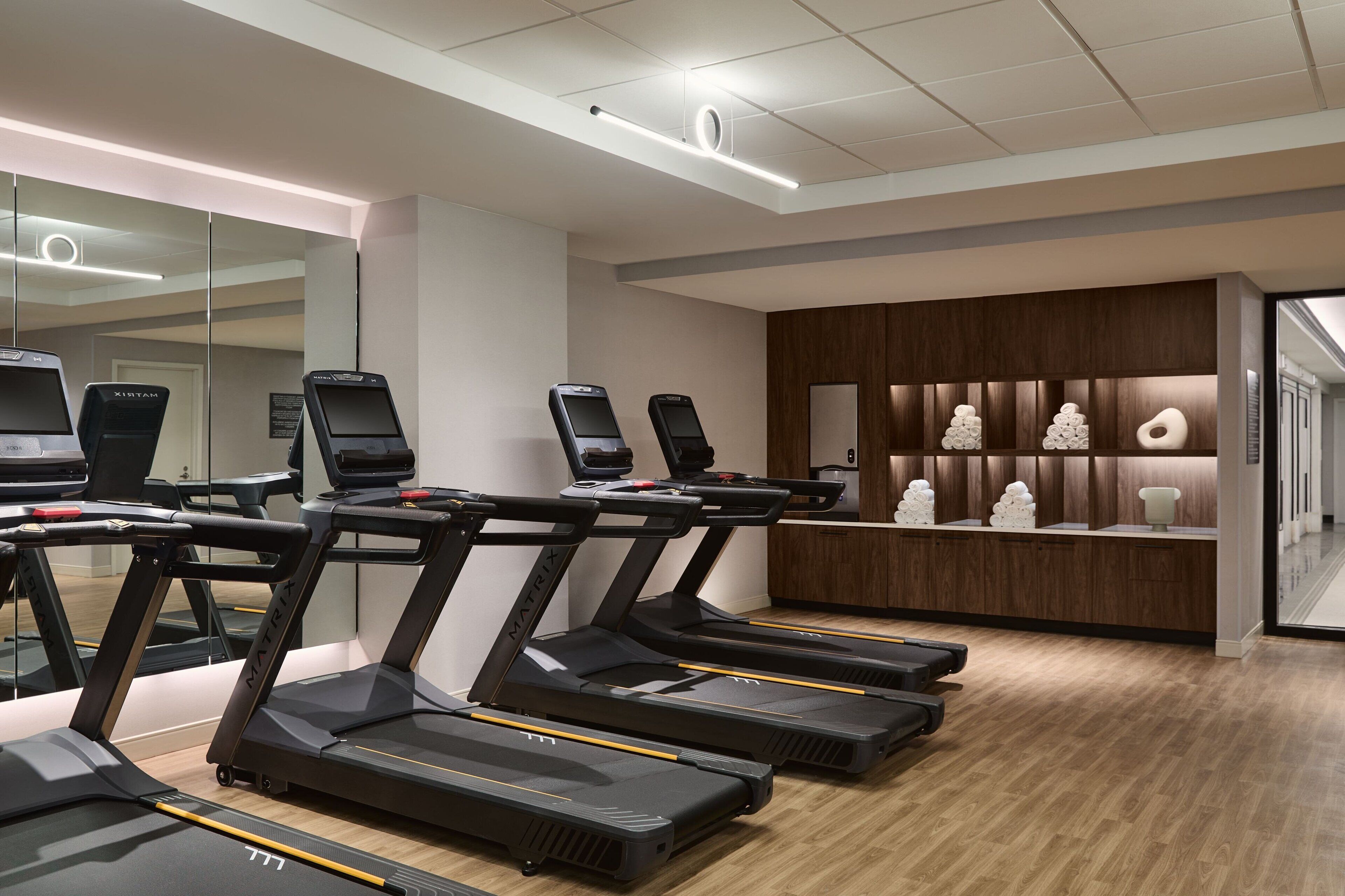 Un gimnasio moderno con cintas de correr, una recepción y una pared de madera con elementos decorativos.