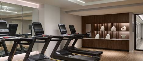 A modern gym with multiple treadmills, a reception desk, and a wooden wall with decorative items.