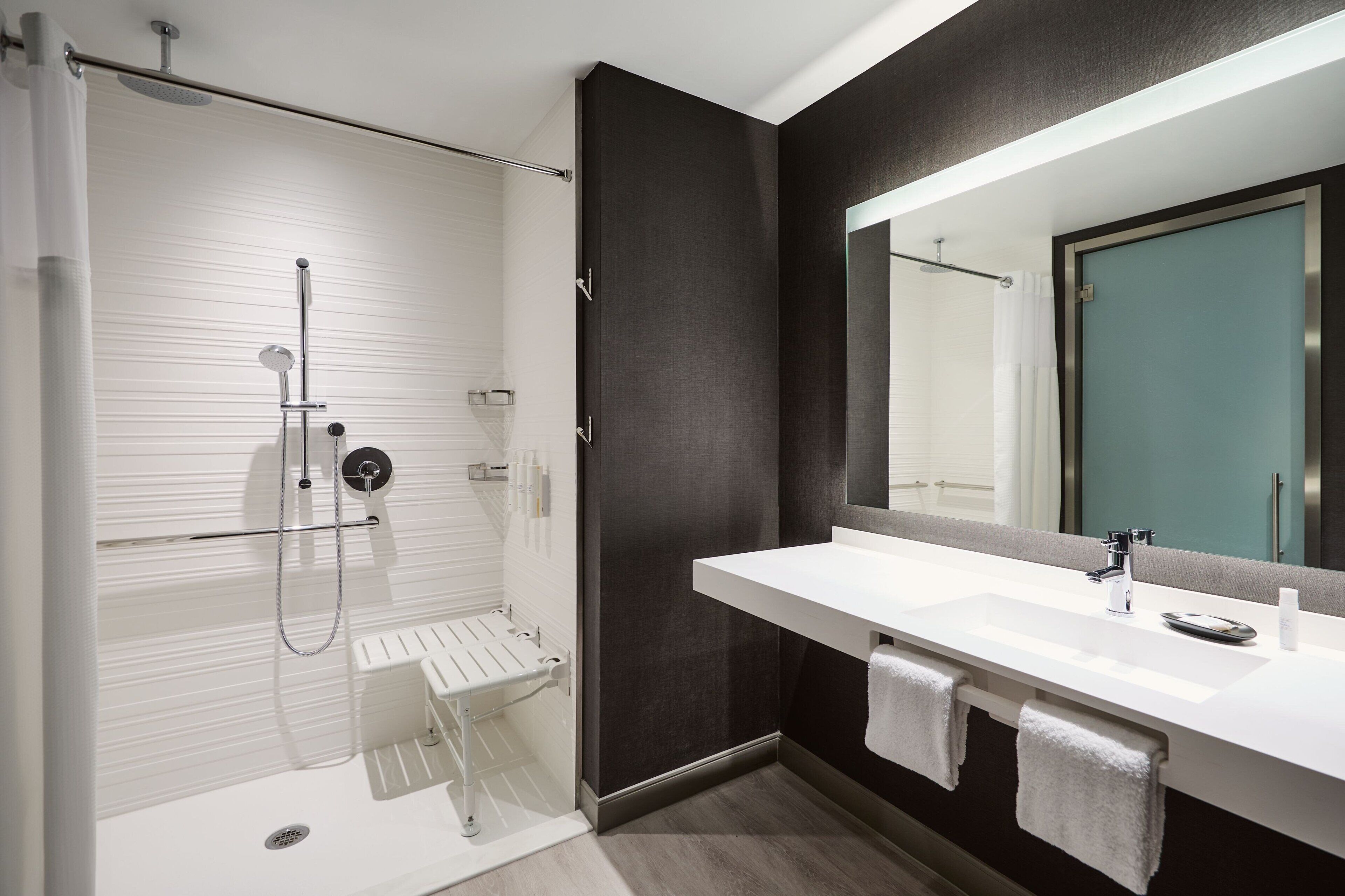 A modern bathroom with a large mirror, white sink, and shower area.