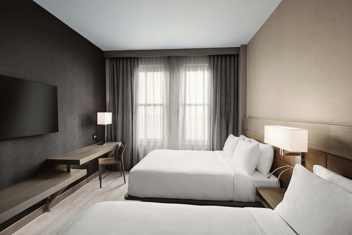 Une chambre d’hôtel moderne, dotée d’un grand lit, d’un bureau, d’une chaise et d’un téléviseur fixé au mur.