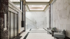 A marble-floored lobby with a central staircase, a freestanding column, and a seating area with a small table and chairs. - AC Hotel by Marriott Kansas City Downtown (Kansas City)