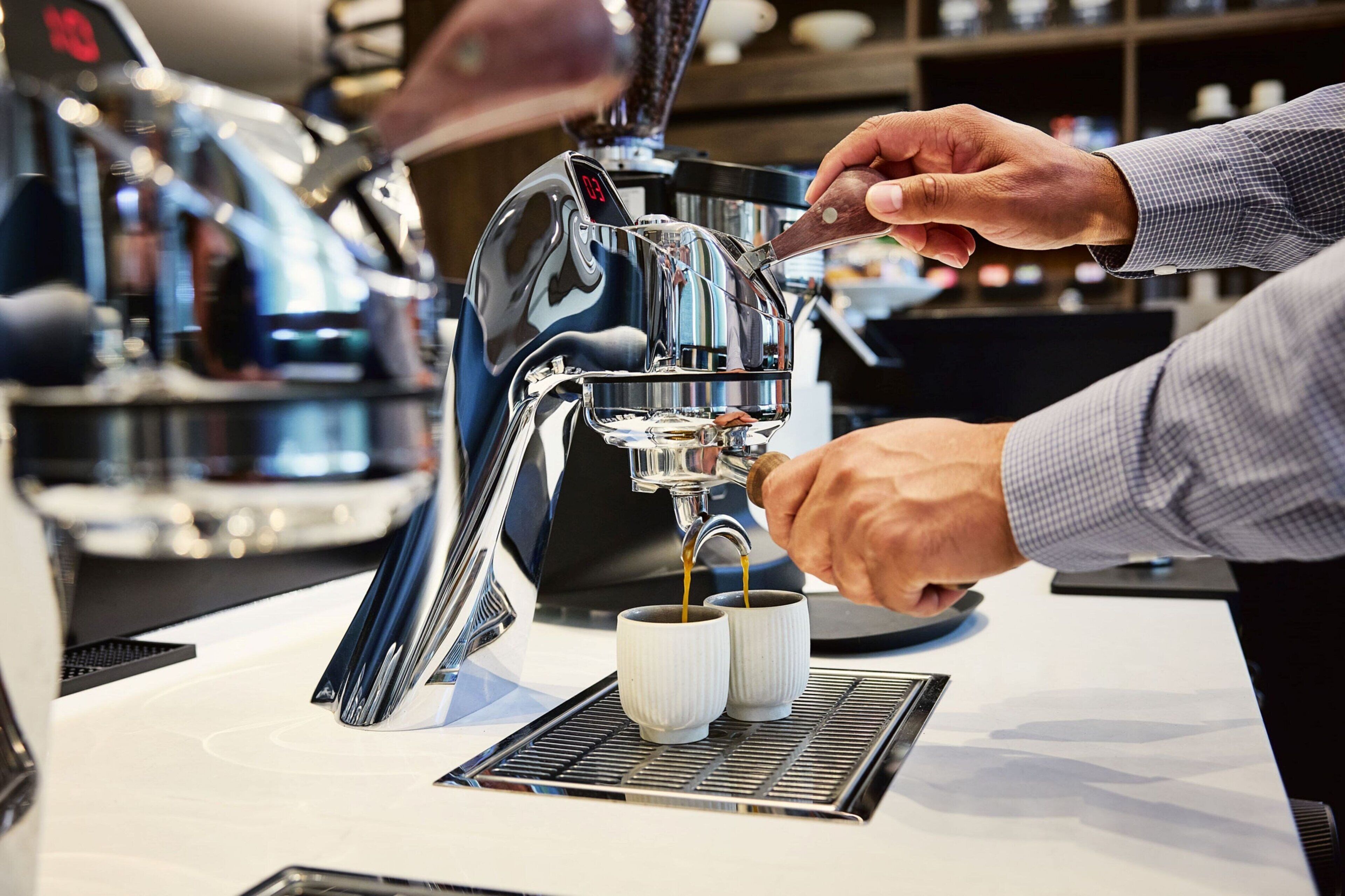 Una persona operando una máquina de café, sirviendo café en dos tazas.
