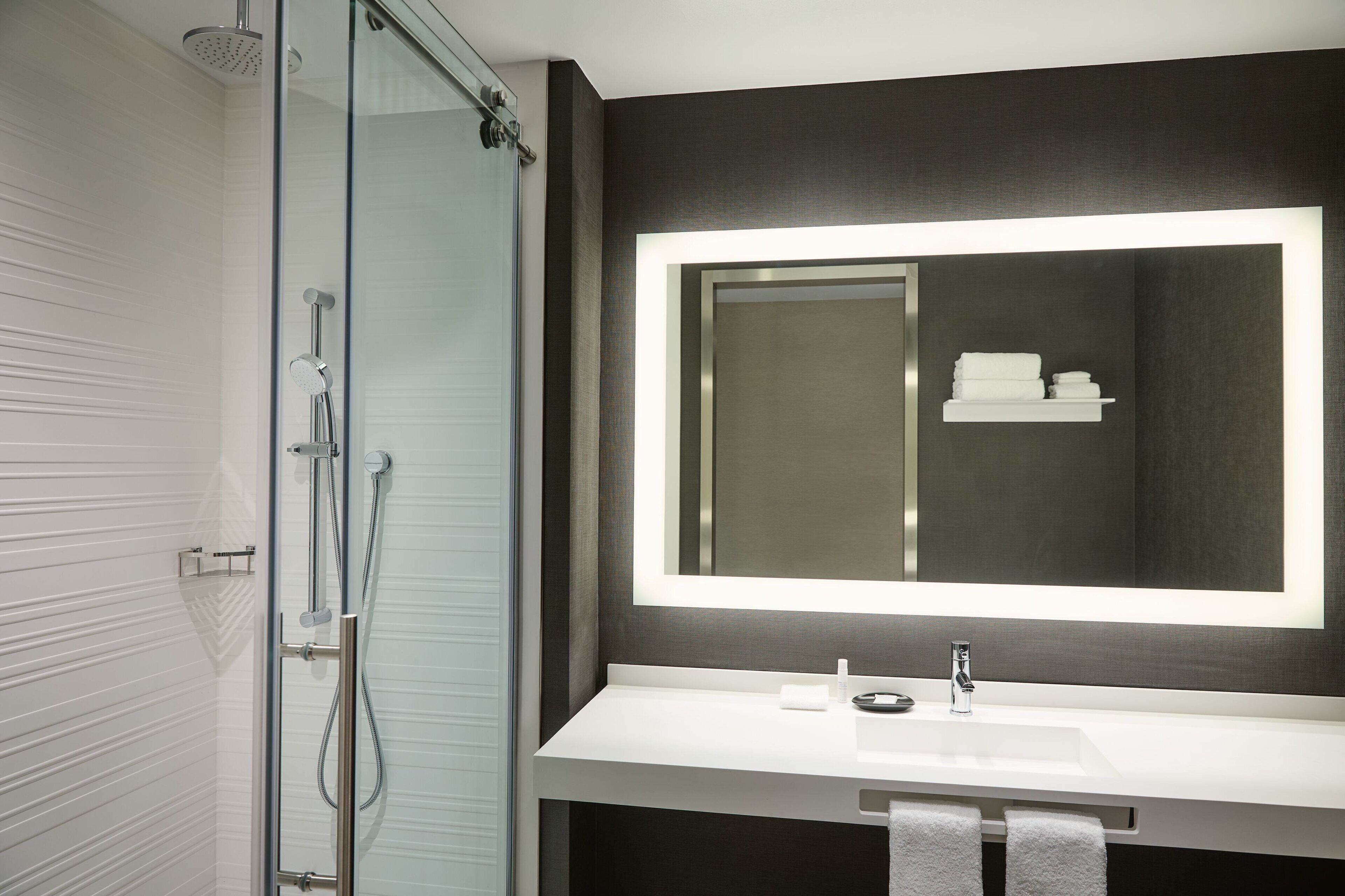 Een moderne badkamer met een douchecabine van glas, een wit wastafelmeubel en een grote spiegel met ingebouwde verlichting.
