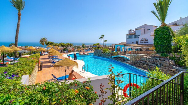 Zona de piscina en un resort con vista despejada al mar, sillas de descanso y un muro de piedra.