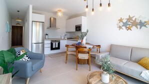 Una sala de estar moderna con sofá, una mesa de comedor con sillas y una cocina con refrigerador y microondas.