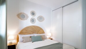 Un dormitorio ordenado con una cama grande, dos mesitas de noche con lámparas y un armario.