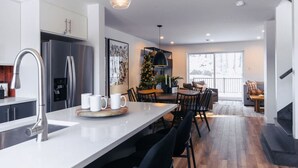 Une cuisine moderne dotée d’un îlot central, d’appareils électroménagers en acier inoxydable et d’un coin repas agrémenté d’un sapin de Noël.