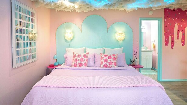 Quarto com uma cama grande, janela com grade e parede com desenho rosa e branco.