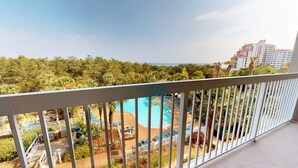 A pool area with lounge chairs and a fenced deck, surrounded by greenery and overlooking a body of water. - Summit 0409 (Miramar Beach)
