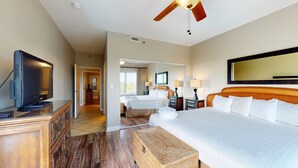 A hotel room with a large bed, a television, a ceiling fan, a bathroom with a mirror, and a hallway leading to another room. - Summit 0409 (Miramar Beach)