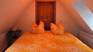Un dormitorio con techo inclinado, puerta de madera y cama con ropa de cama naranja.