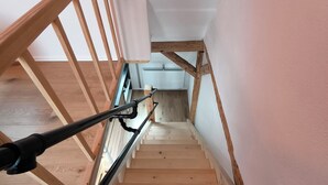 Una escalera de madera con barandilla que lleva a un rellano con una pared blanca y un radiador.
