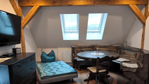 Un dormitorio tipo loft con techo de madera, televisor, una mesa redonda y dos ventanas.