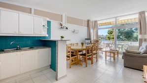A modern kitchen with white cabinets, a teal backsplash, and a dining area with wooden chairs and a table. - RESIDENCIAL ALMADRAVA 4  Roses (Rosas / Roses)
