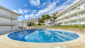 A swimming pool surrounded by modern buildings with balconies, a clear sky, and a hilly backdrop. - RESIDENCIAL ALMADRAVA 4  Roses (Rosas / Roses)